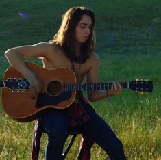 a shirtless man sitting in a chair playing an acoustic guitar