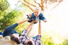 a man holding a baby up in the air while another person holds him upside down