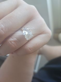 a woman's hand with a diamond ring on top of her finger, in front of a window