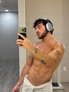 a shirtless man taking a selfie with his cell phone and headphones on