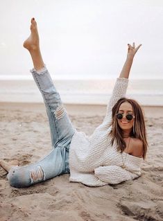 a woman laying on the beach with her legs up in the air and wearing sunglasses