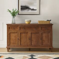 a wooden sideboard with two bowls on top and a basket next to it in front of a painting