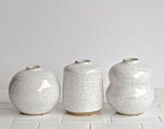 three white vases sitting on top of a tiled floor