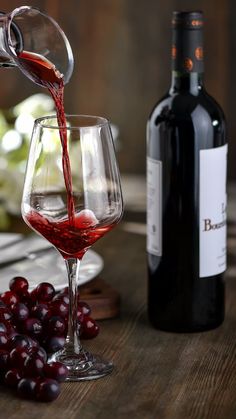 red wine being poured into a glass next to grapes