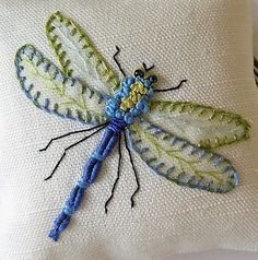 a blue and green dragonfly sitting on top of a white pillow with stitching