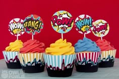 cupcakes decorated with colorful icing and pop - art decorations are displayed in front of a red background