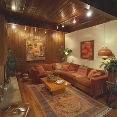 a living room filled with furniture and wooden paneled walls, along with potted plants