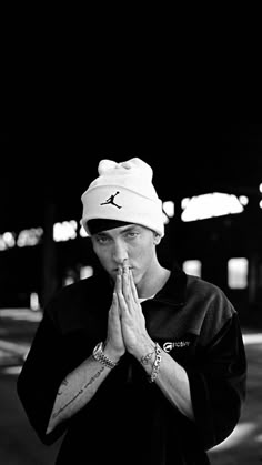 a young man wearing a hat and praying with his hands folded in front of him