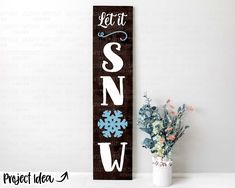 a wooden sign that says let it snow next to a potted plant on a table