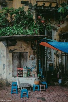 an old run down building with blue chairs and tables in front of it on a brick sidewalk