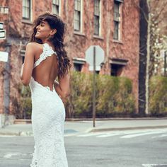 a woman in a white wedding dress is standing on the street and looking at something