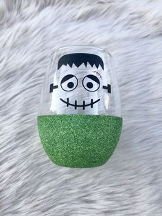 a glass with a face painted on it sitting on top of a fur covered surface