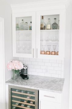 a kitchen with white cabinets and marble counter tops, wine bottles in the cabinet doors