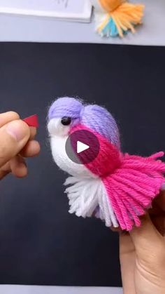 a person is holding a small bird made out of yarn and yarnsticks that are pink, white, and purple