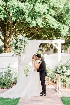 a bride and groom kissing in front of an outdoor wedding ceremony arch with white flowers