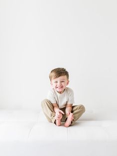 a little boy sitting on top of a white mattress smiling at the camera with his hands in his pockets