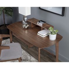 a wooden desk with a lamp on it and a plant in the corner next to it