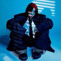 a woman with red hair sitting on the ground wearing black shoes and a blue background