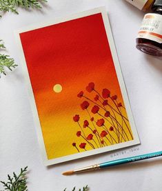 an orange and yellow card with red flowers on it next to some watercolor paints