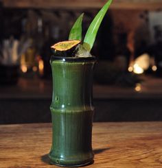 a green drink in a tall glass sitting on top of a wooden table