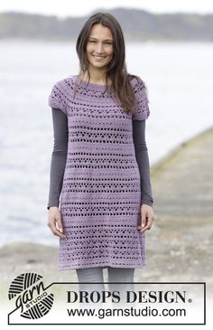 a woman standing next to the water wearing a purple crochet dress and smiling