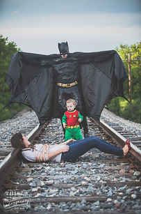 a woman laying on train tracks next to a bat costume and a man dressed as batman