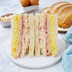 there is a sandwich cut in half on a plate with eggs and bread behind it