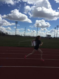 a woman running on a track in the middle of a field with clouds above her