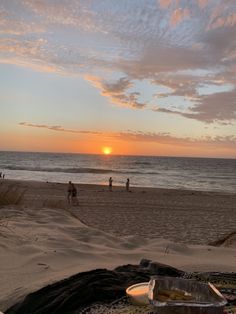 the sun is setting at the beach with people on it