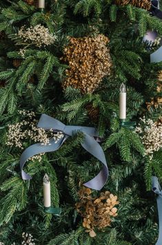 a christmas tree with blue ribbon and candles on it, surrounded by pine cones and baby's breath