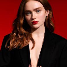 a woman with red hair wearing a black suit and holding her hands on her chest