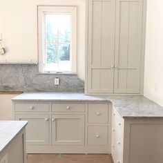 an empty kitchen with marble counter tops and white cupboards on either side of the window