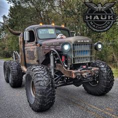 an old truck with huge tires driving down the road