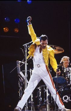 a man in yellow jacket and white pants on stage with his hands up to the side