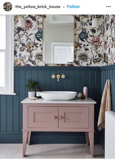 a bathroom with floral wallpaper and a pink vanity topped with a white bowl sink