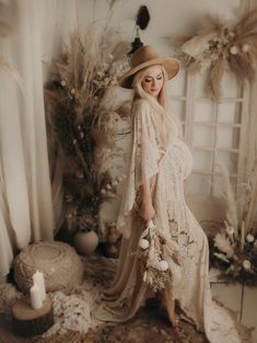 a woman in a long dress and hat poses for a photo with feathers on the floor