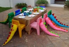 a table set up with colorful plastic dragon chairs and plates on top of the table