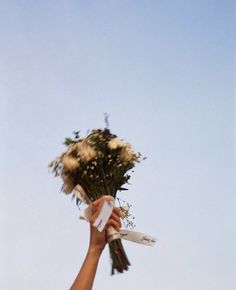 a person holding flowers up in the air with a blue sky behind them on a sunny day