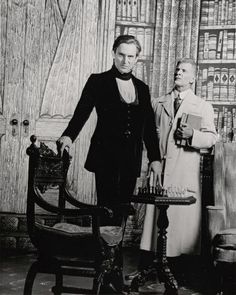 an old black and white photo of two people standing in front of a bookcase