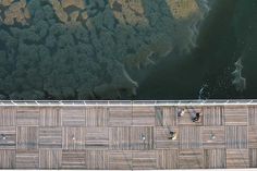 an aerial view of two people walking on a boardwalk next to the water and trees