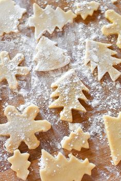 some cut out cookies are on a wooden table with powdered sugar and sprinkles