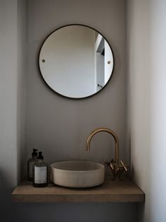 a bathroom sink with a round mirror above it and a soap dispenser