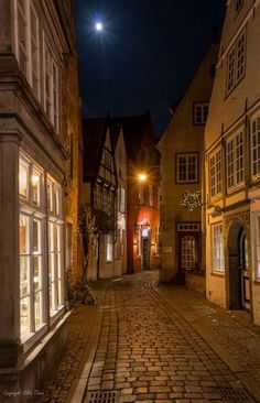 an empty cobblestone street at night with the moon in the sky