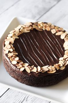 a chocolate cake on a white plate topped with sliced almonds and dark chocolate frosting