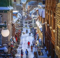 people are walking down an alley way in the winter with snow on the ground and buildings