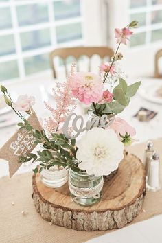 flowers are in mason jars on a wood slice at the center of a dining room table