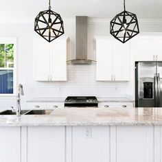 a kitchen with white cabinets and marble counter tops, two pendant lights over the island