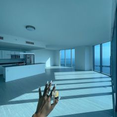 a person's hand reaching out towards an empty room with large windows and floor to ceiling windows