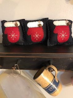 three black and red christmas mittens are sitting on a shelf next to a coffee mug