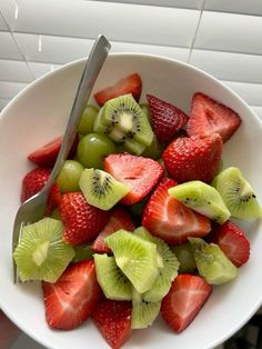 a white bowl filled with sliced kiwis and strawberries next to a fork